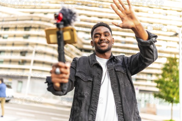 African man vlogger waving at camera while recording video blog in the city