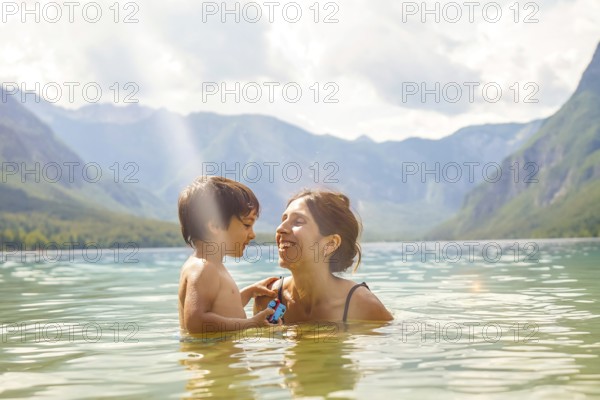 Mother and son enjoying summer holidays, playing in the refreshing water of lake bohinj, surrounded by the stunning julian alps