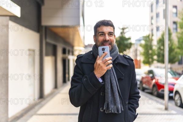 Adult caucasian man in winter elegant clothes sending voice message while walking along the street
