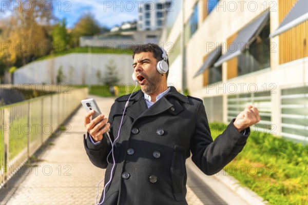 Happy adult man in elegant clothes enjoying listening to music, singing and dancing at city in winter