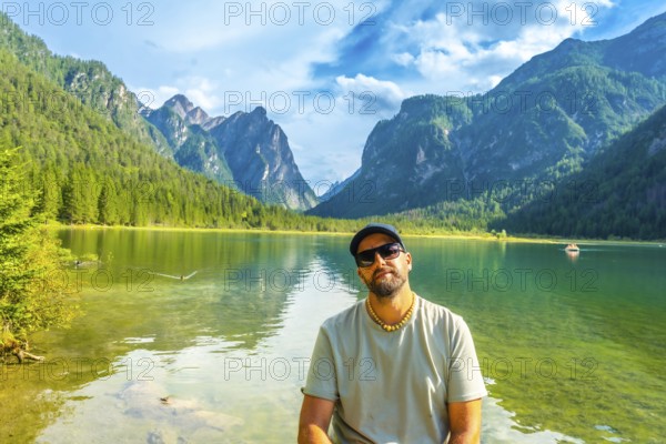 Tourist relaxing by lake dobbiaco, surrounded by the stunning peaks of the dolomites on a beautiful summer day in italy