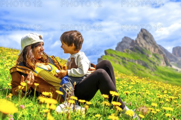 Tourists relaxing in a dandelion field, enjoying the view of the seceda mountains in the italian dolomites during a sunny summer day