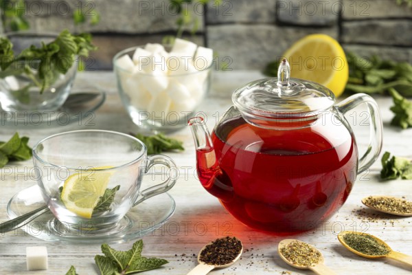 Touched teapot, glasses with mint, sugar pieces, different types of tea and lemons