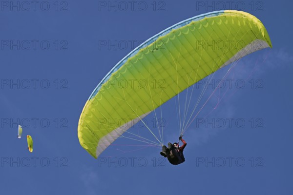 Paraglider pilot with green and yellow paraglider flies in the blue sky