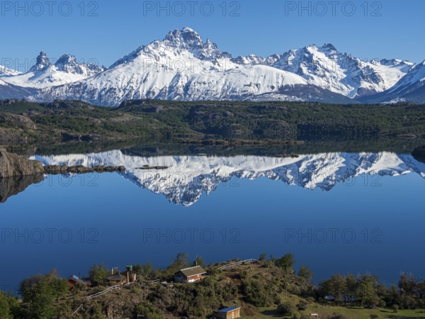 The snow-covered Mt. Cerro Castillo is reflected in a lake, small farm by the lake, Patagonia, Chile, South America