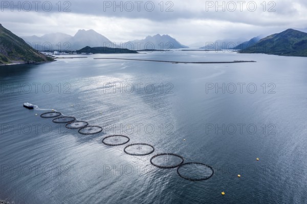 Aerial view of a salmon farm, rainy weather, grey sky, village Myre in the back, Vesteralen islands, Norway, Europe
