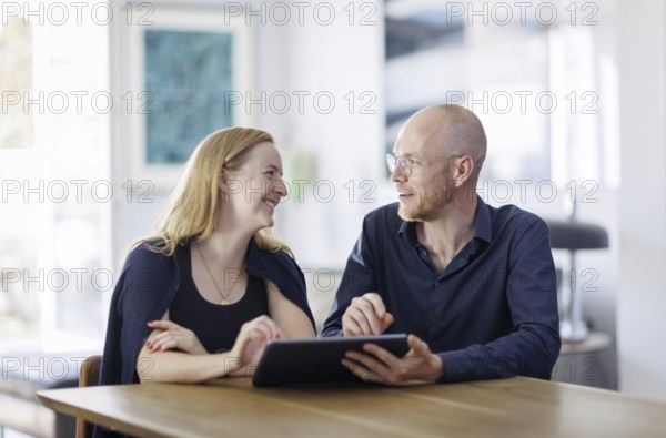 Symbolic photo. A woman and a man sit together at a table with a tablet and talk. Berlin, 13.08.2024
