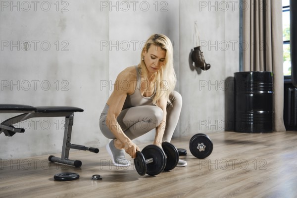 Middle-aged woman athlete adding weights to dumbbells in the gym
