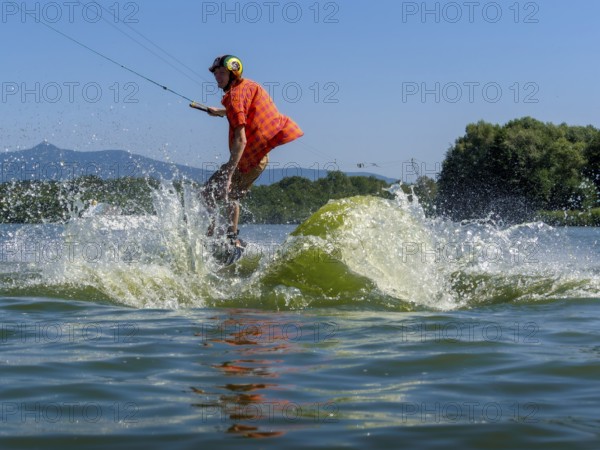 Young casual man with flapping shirt on wakeboard jumping into the lake, water ski and wakepark, Stráž pod Ralskem, Czech Republic, Europe