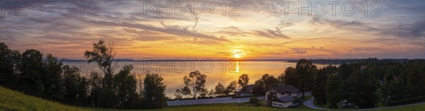 Sunset over a lake with a calm atmosphere, surrounded by trees and a slightly cloudy sky, Chiemsee