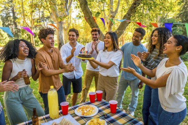 Happy young caucasian woman carrying a birthday cake while celebrating birthday in a park with multi-ethnic friends