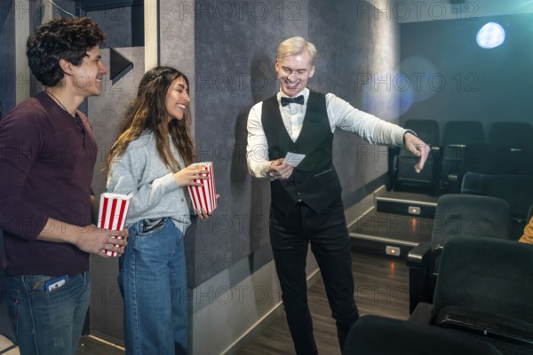 Young couple holding popcorn buckets while usher showing their seats in a movie theater, ready to enjoy the film
