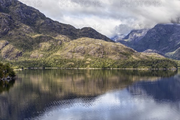 Calm ocean with clear reflection of forested mountains and cloudy skies in a peaceful setting, Chile, South America