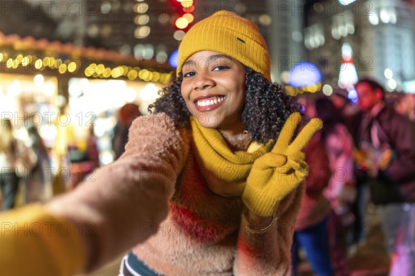 Smiling young woman wearing yellow winter clothes takes a selfie at christmas market showing peace sign with fingers