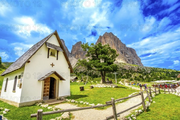 Tourists enjoying a sunny day at sella pass, with the chapel and the sassolungo group in the background