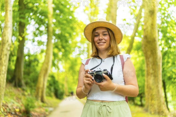 Portrait of a caucasian female young photographer standing in the forest smiling at camera and holding a camera