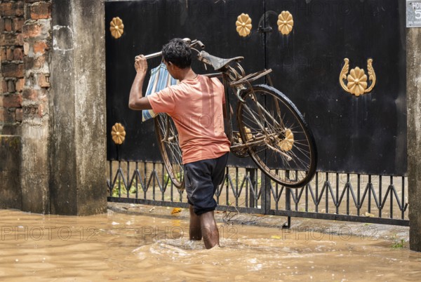 A person carries a bicycle as he wade through a flooded street after heavy rains in Guwahati, India on April 28, 2025
