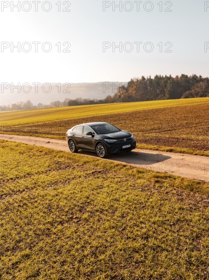A car drives alone on a country lane, surrounded by golden fields under the sun, electric car VW ID5, Deer Carsharing, Gechingen, Black Forest, Germany, Europe