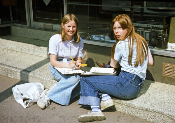 Secondary school girls doing fieldwork in geography, United Kingdom 1970s two teenagers with clipboards sitting outside a shop 1977