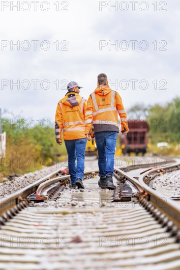 Two men in orange work clothes walking on rails, a wagon in the background, track construction Hermann Hesse railway, Calw district, Black Forest, Germany, Europe
