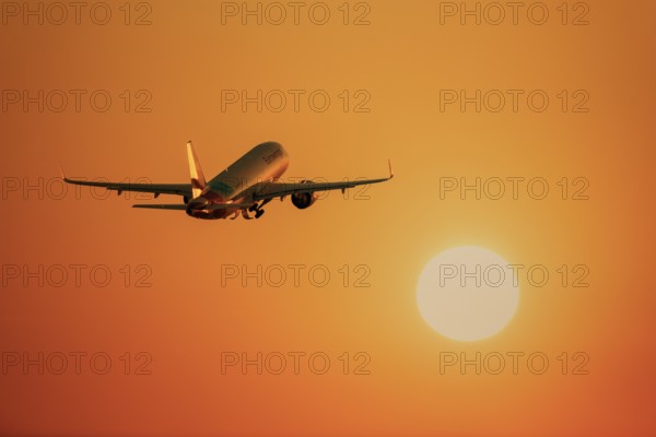 An aeroplane flies towards a large, orange glowing sun in the clear sky, take-off, Baden-Württemberg, Germany, Europe