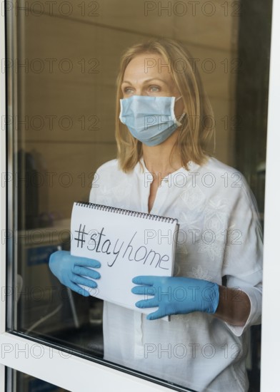Woman with medical mask holding stay home notebook window