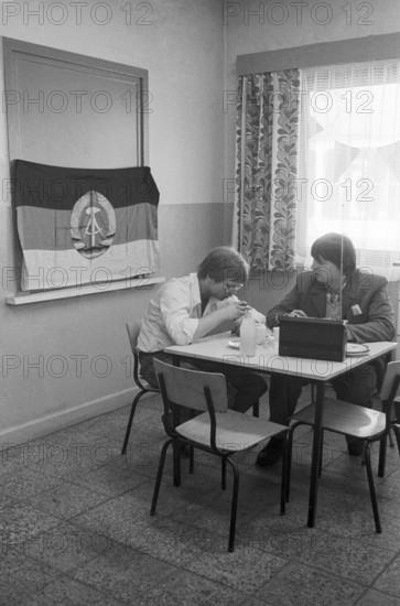 23/09/1982 GDR East Berlin Mitte district. Two tram drivers are taking a break in a canteen of the Berlin transport company. A GDR flag on the wall. A portable radio on the table. Berlin