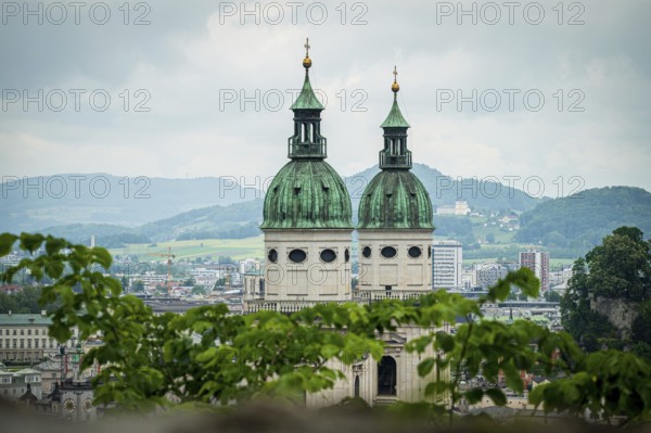 Two church towers with green roofs, framed by leaves, landscape in the background, Salzburg, Austria, Europe
