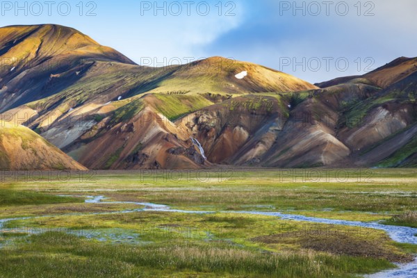 Green Valley is flooded with melt water. Snow lies in the hollows of colorful rhyolite mountains. Early summer morning in the National Park Landmannalaugar, Iceland, Europe