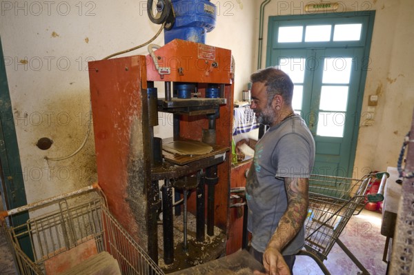 A man operates a brick press in a workshop, bricks and metal machine visible, Brickworks Patmos Cotto, Traditional brick making, Kampos, Patmos, Dodecanese, Greek Islands, Greece, Europe