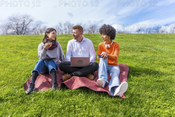 Three young entrepreneurs working outdoors, using technological devices, enjoying a sunny spring day