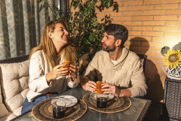 Smiling man and woman sharing a meal of burgers and drinks, creating a warm and intimate atmosphere on their balcony