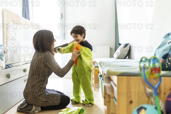 Mother helping her son put on a dinosaur costume, preparing for imaginative play in a cozy bedroom