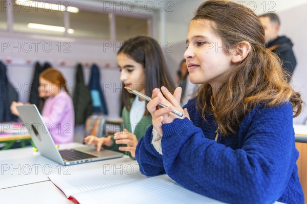 Smart young female students thinking and learning using laptop computer and notebook in elementary school classroom