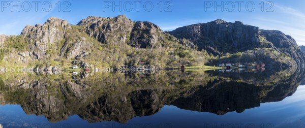 Near Ana-Sira at the norwegian southern coast, lonely houses at the foot of a rock formation are reflected in the calm sea, panorama, Norway, Europe
