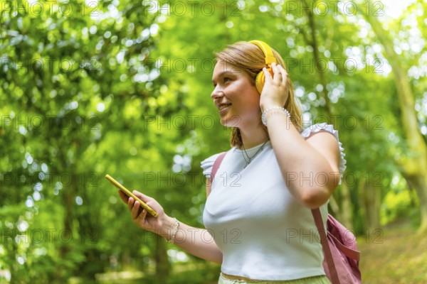 Happy caucasian young woman using phone and enjoying music in the nature while trekking in the forest