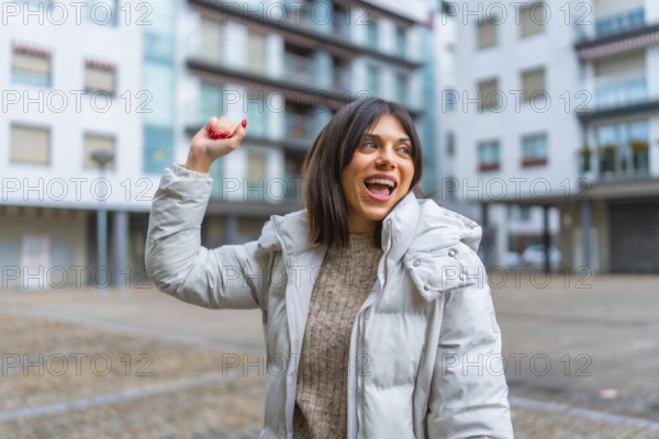 Happy woman wearing winter jacket raising hand while dancing in the city