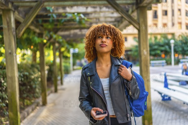 Latin young woman walking with rucksack while using smartphone to find a direction in the city