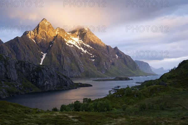 Mountain landscape in the Lofoten Islands. View across the Maervollspollen fjord to mountains in the night sunlight. At night at the time of the midnight sun, clouds and sun. Mountain peaks in the sunlight. Early summer. Vestvagoya, Lofoten, Norway, Europe