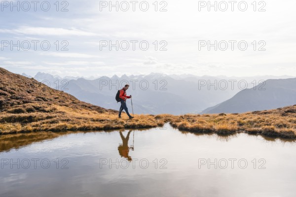 Mountaineer hiking with poles, reflected in a small mountain lake on the Krahberg, mountain panorama in autumn, Venet crossing, Ötztal Alps, Tyrol, Austria, Europe