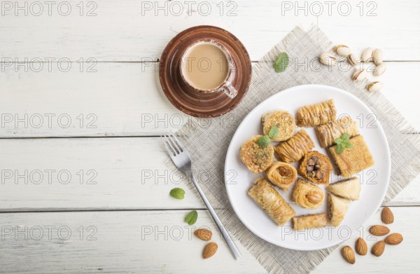 Traditional arabic sweets (kunafa, baklava) and a cup of coffee on a white wooden background and linen textile. top view, flat lay, copy space