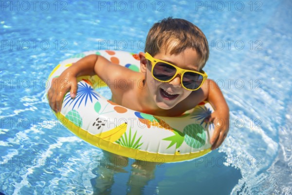 Boy having fun in the swimming pool with a floating rubber ring in summer