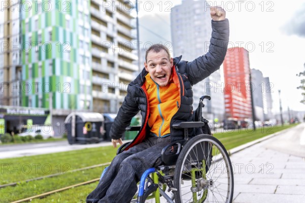 Happy disabled man celebrating raising his fist while sitting in a wheelchair in a city street