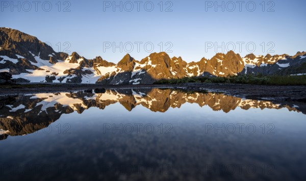 Rocky mountain peaks reflected in a small pond, mountain landscape with alpenglow at sunrise, at the Trollfjord Hytta, at the Trollfjord, Lofoten and Vesterålen, Nordland, Norway, Europe