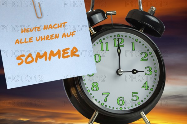(Photomontage) Summer time changeover Symbolic image: Alarm clock in front of evening sky and text TODAY NIGHT ALL CLOCKS TO SUMMER