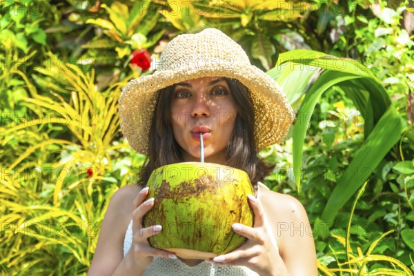 Young woman with straw hat savoring refreshing coconut water, surrounded by vibrant tropical foliage in siargao island, philippines
