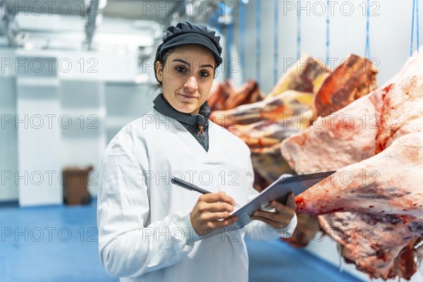 Female butcher making quality report writing notes in a clipboard in meat processing factory