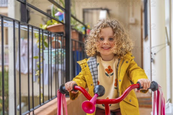 Close-up of a smiling little girl playing riding bike in the terrace at home