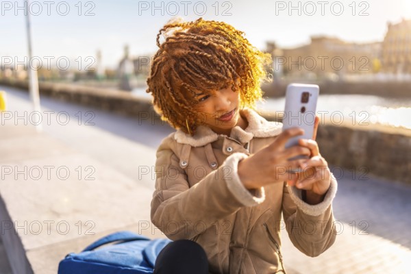 Latin young woman taking photo with mobile phone of a beauty sunset on the river in the city