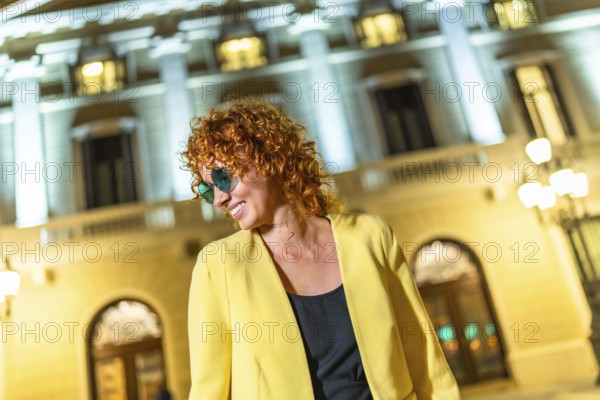 Frontal view of a stylish woman wearing casual yellow jacket and sunglasses looking aside in the city at night
